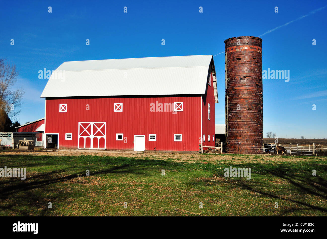 A modern red barn topped by a corrugated steel roof with an unusual brick silo in rural northern Illinois, USA. Stock Photo
