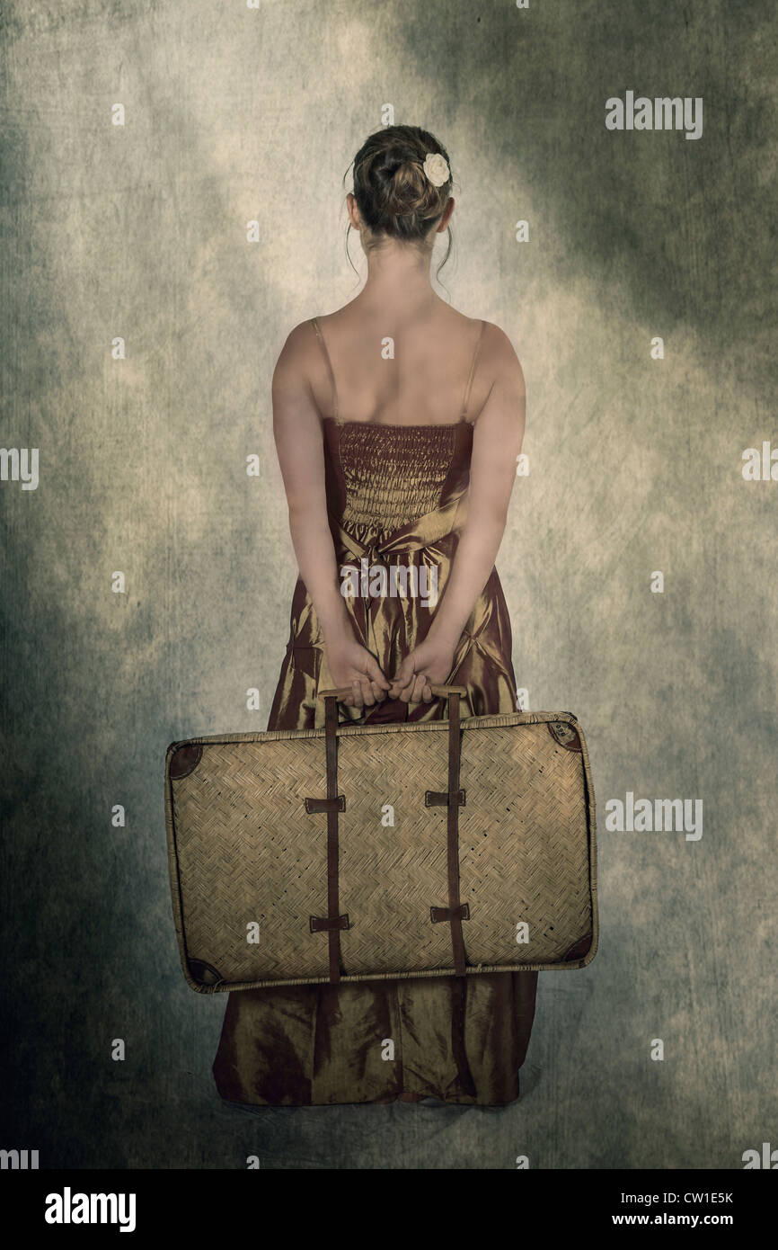 a woman in a period dress holding a small, old suitcase behind her back Stock Photo