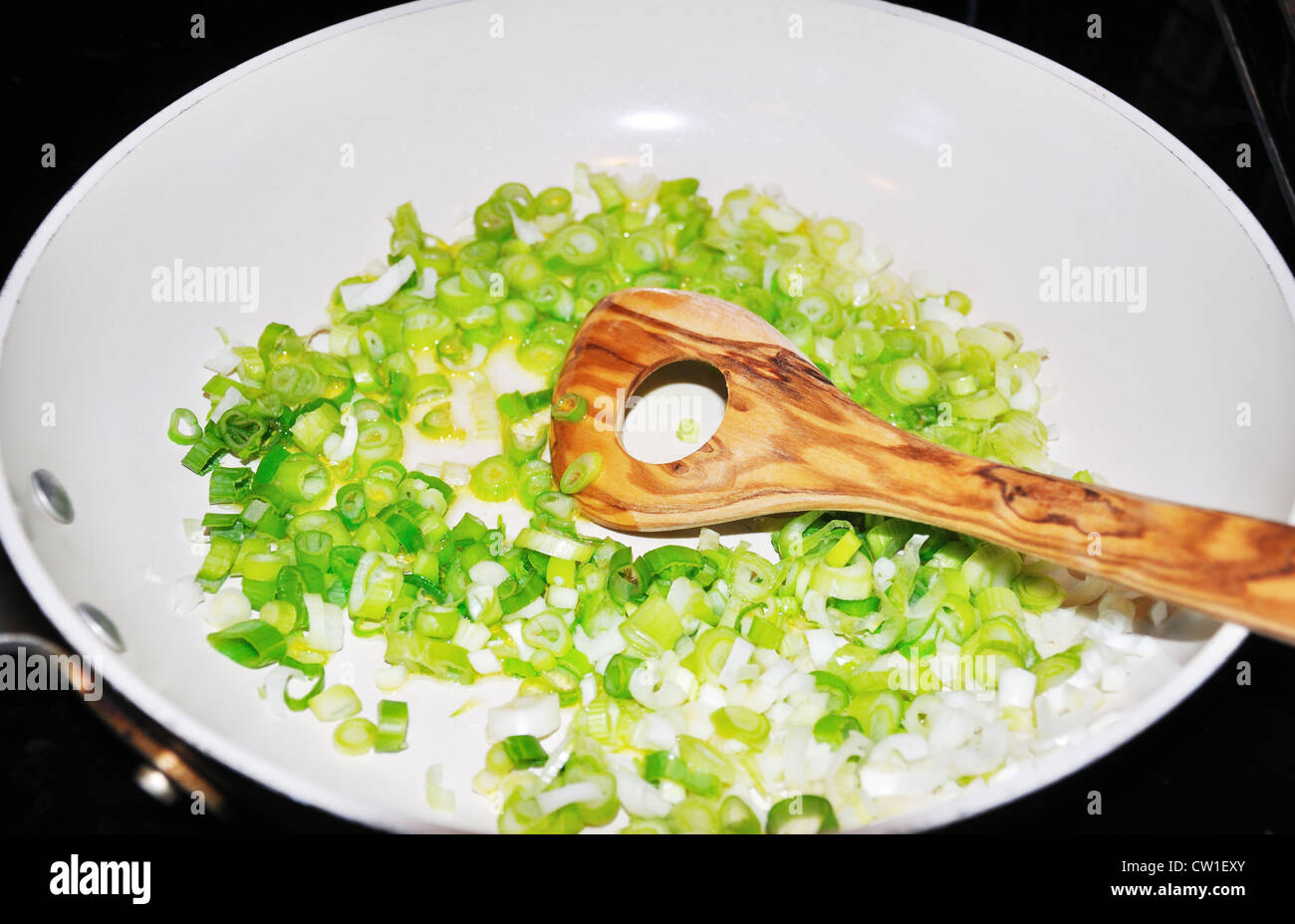 Frying green onions in ceramic enamel frying pan Stock Photo