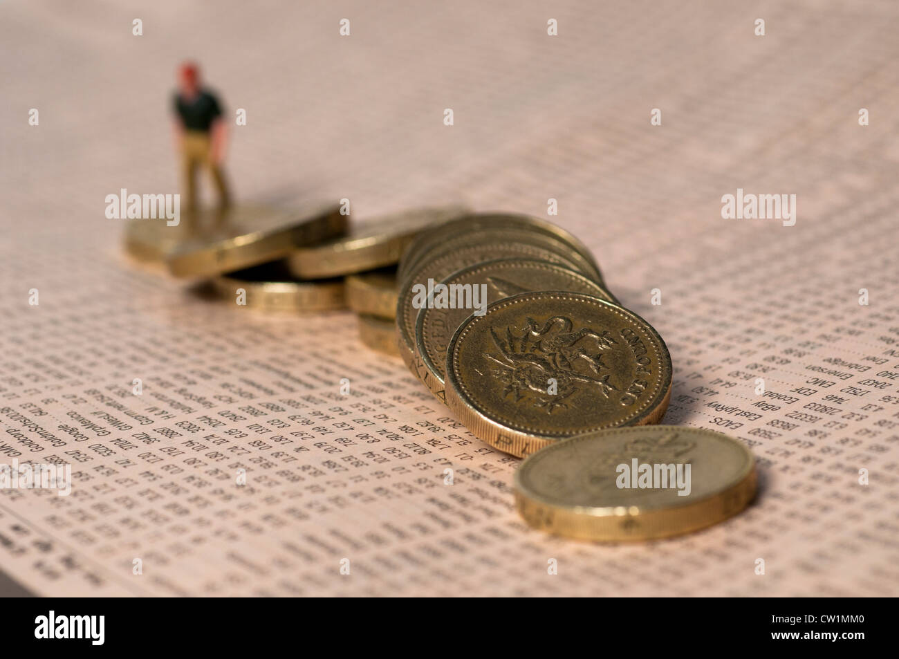 Little figure of a man climbing over tumbled one pound coins laid over share figures, Stock Photo