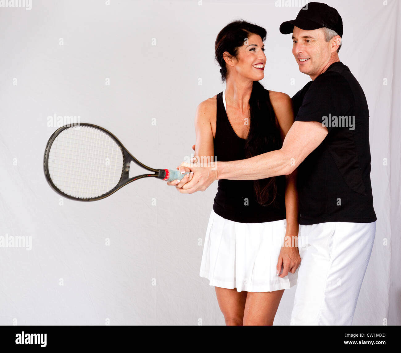 A couple in tennis outfit, he is showing her how to hold the tennis