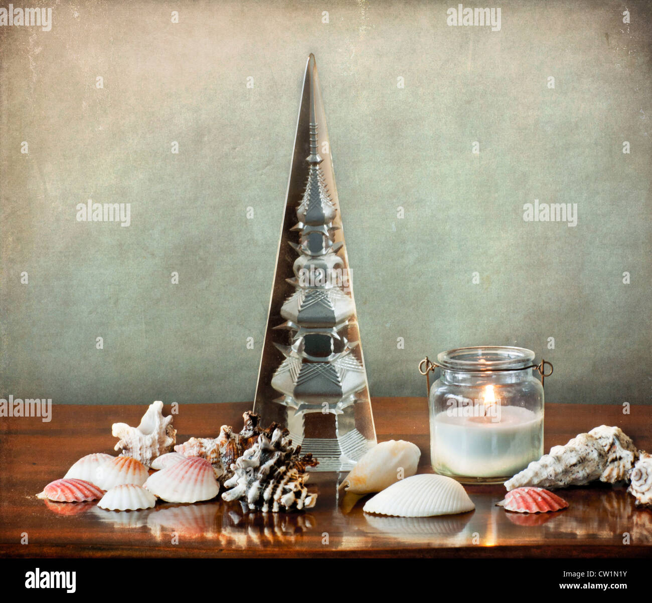 Still life: shells, a glass tower,a lit candle in glass vase on a wooden polished table Stock Photo