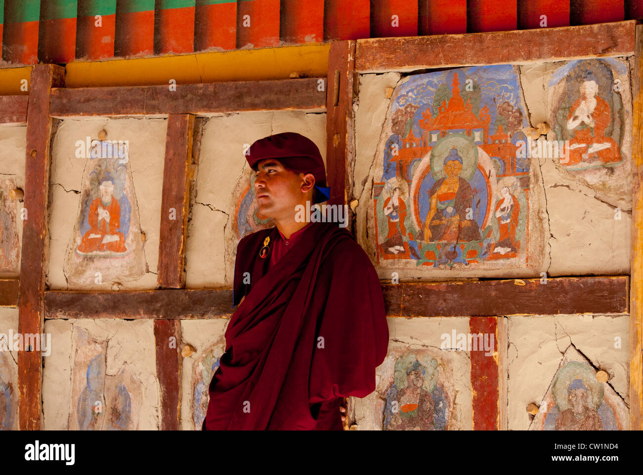 A monk stands in front of a wall covered with paintings of a religious nature at Hemis Monastery, Ladakh, India Stock Photo