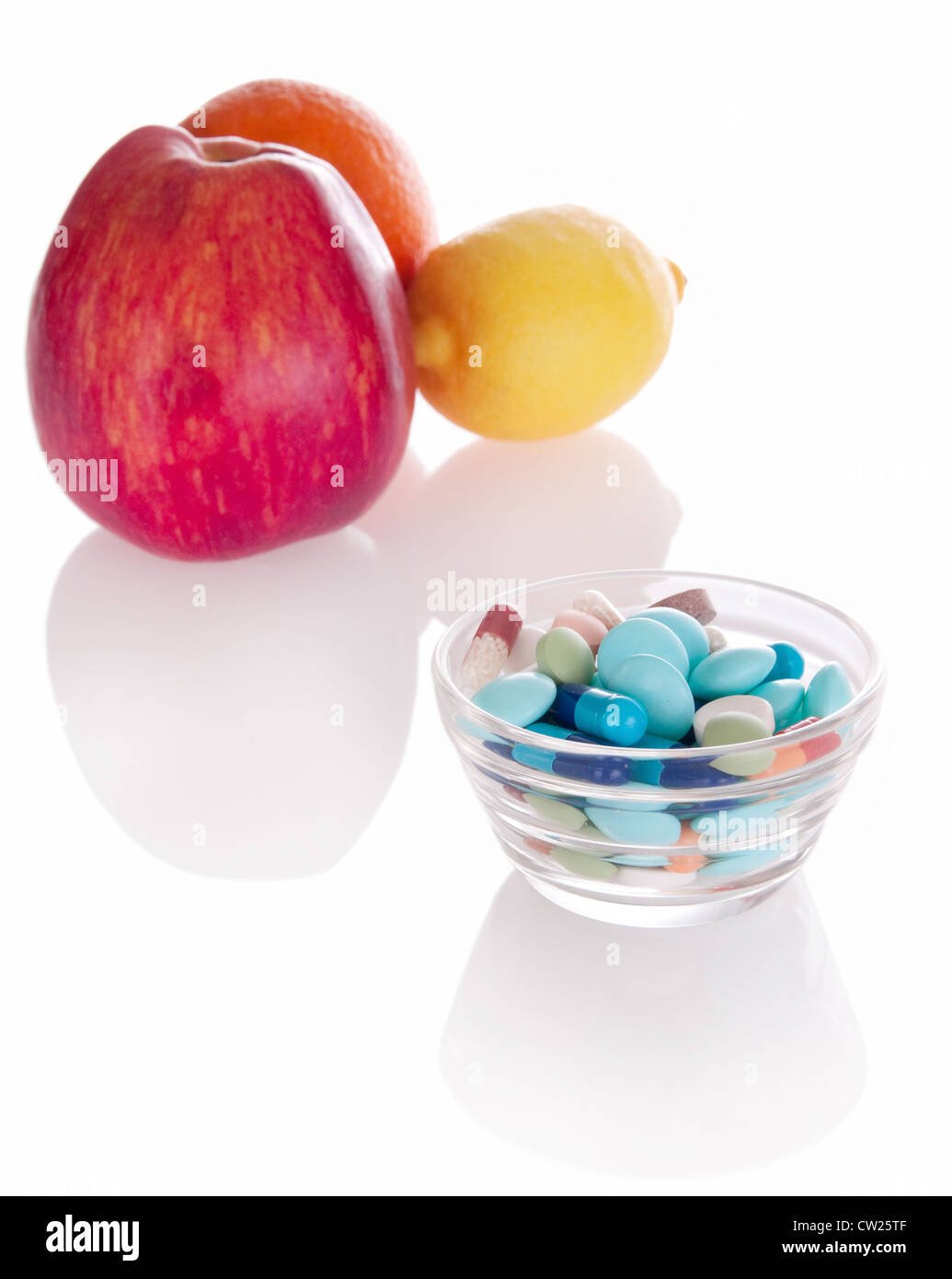Concept of vitamin medicine with different pills in glass bowl and defocused fruits on background with soft shadows Stock Photo