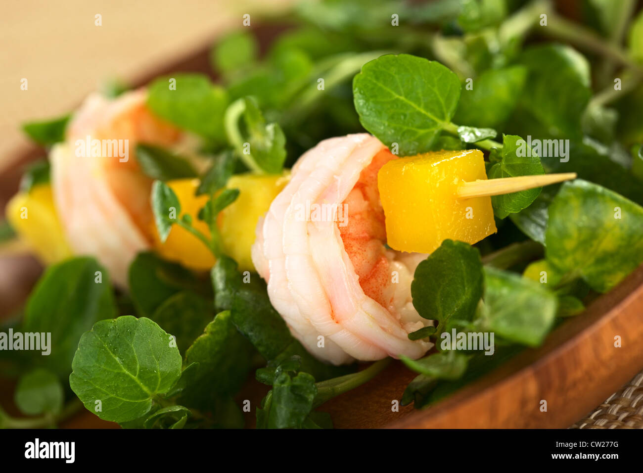 Fresh cooked shrimp, mango and avocado on skewer with watercress leaves on wooden plate Stock Photo