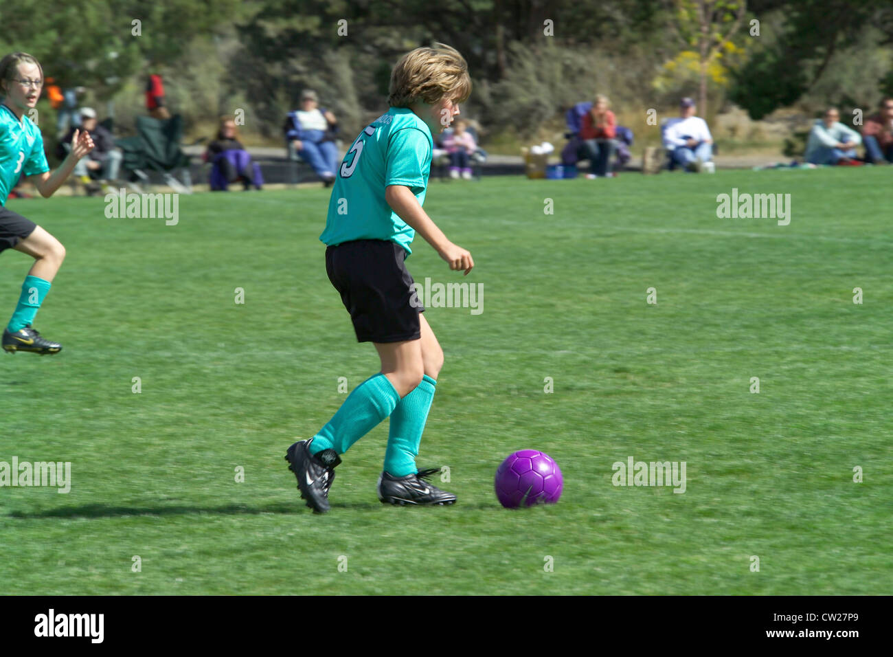 A young girl races across the playing field to kick the soccer ball during an after-school match watched by family and friends in Bend, Oregon, USA. Stock Photo