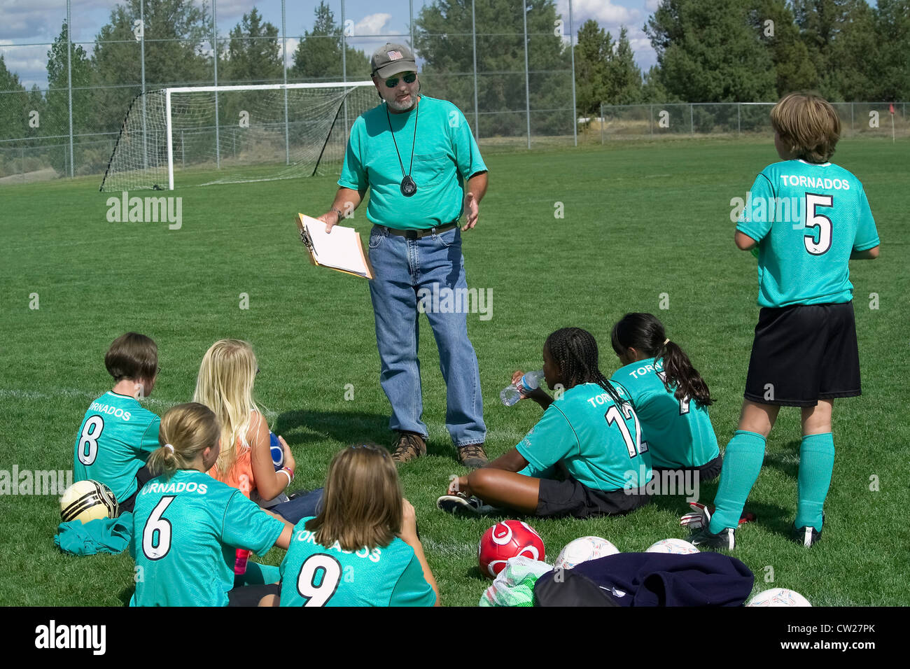 The male coach gives a pep talk while a young girls' team rests on the playing field between after-school soccer matches in Bend, Oregon, USA. Stock Photo