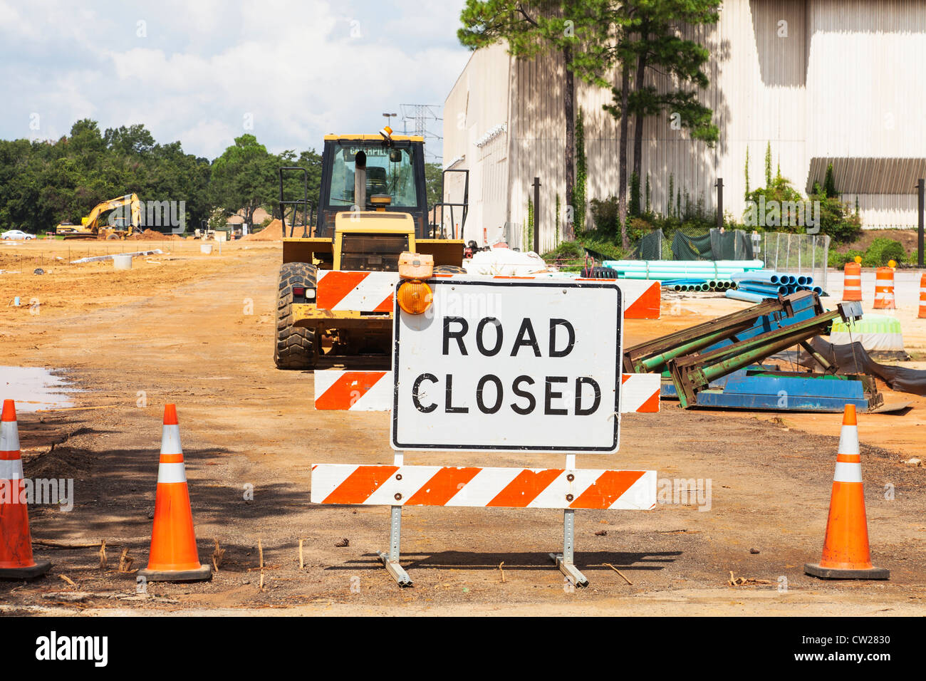 Road closed sign with heavy industrial road building equipment on construction site Stock Photo