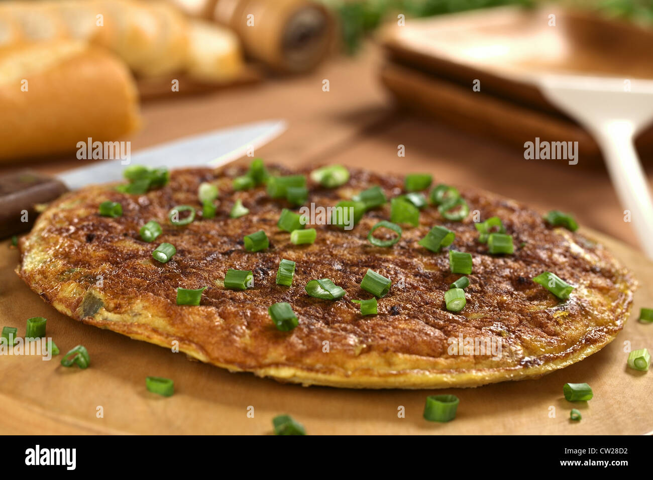 Fresh homemade Spanish tortilla (omelette with potatoes) with green onion on top and bread in the back Stock Photo