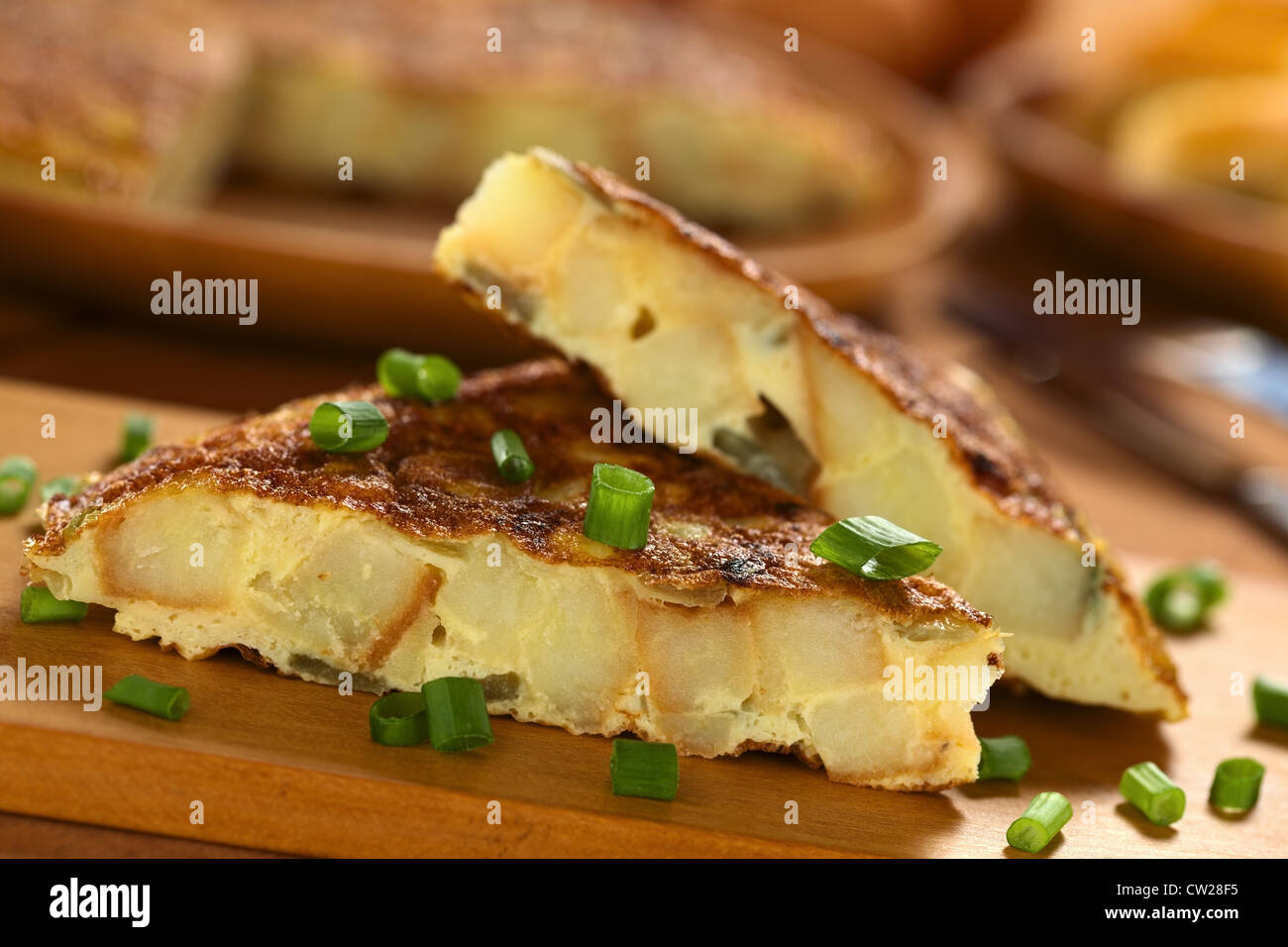 Fresh homemade Spanish tortilla (omelette with potatoes and onions) slices with scallion on top on wooden cutting board Stock Photo