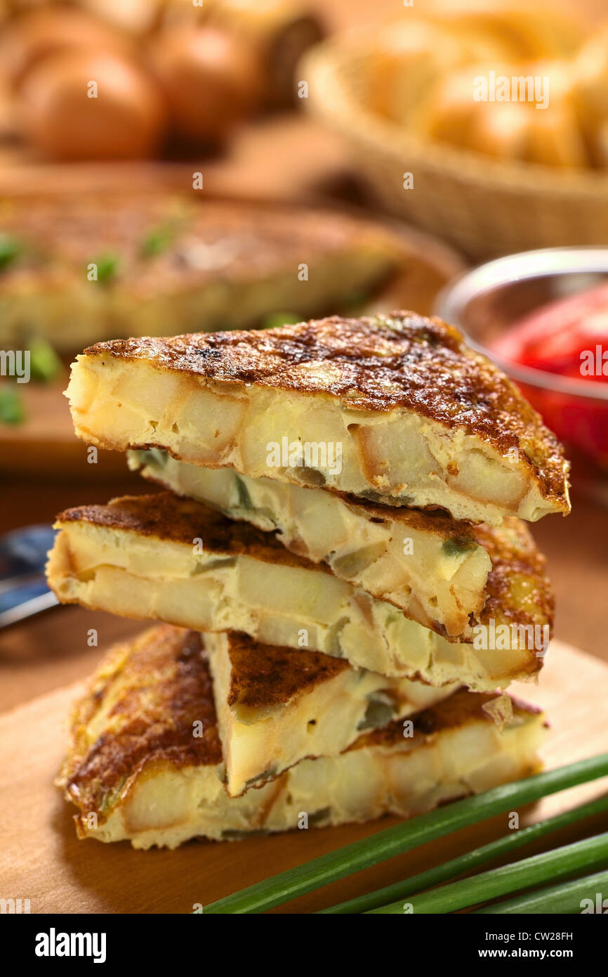 Fresh homemade Spanish tortilla (omelett with potatoes and onions) slices piled on wooden cutting board Stock Photo