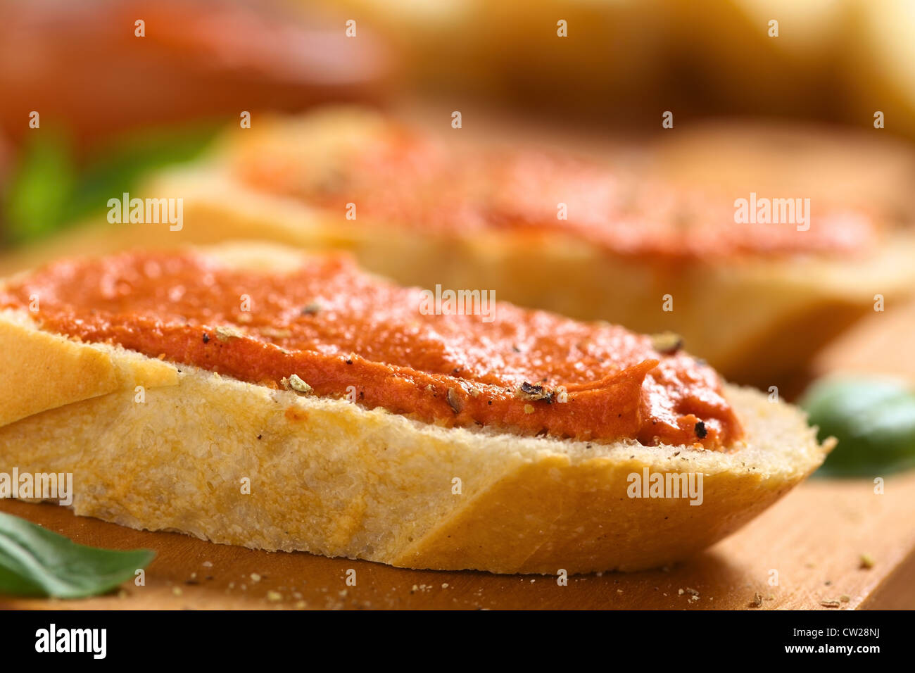 Homemade tomato-butter spread on baguette slices with fresh ground pepper on wooden board Stock Photo