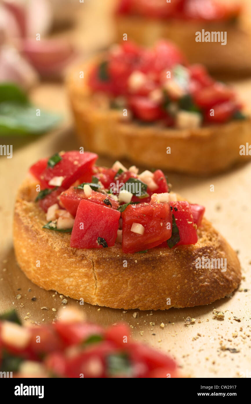 Fresh homemade crispy Italian antipasto called Bruschetta topped with tomato, garlic and basil on wooden board Stock Photo