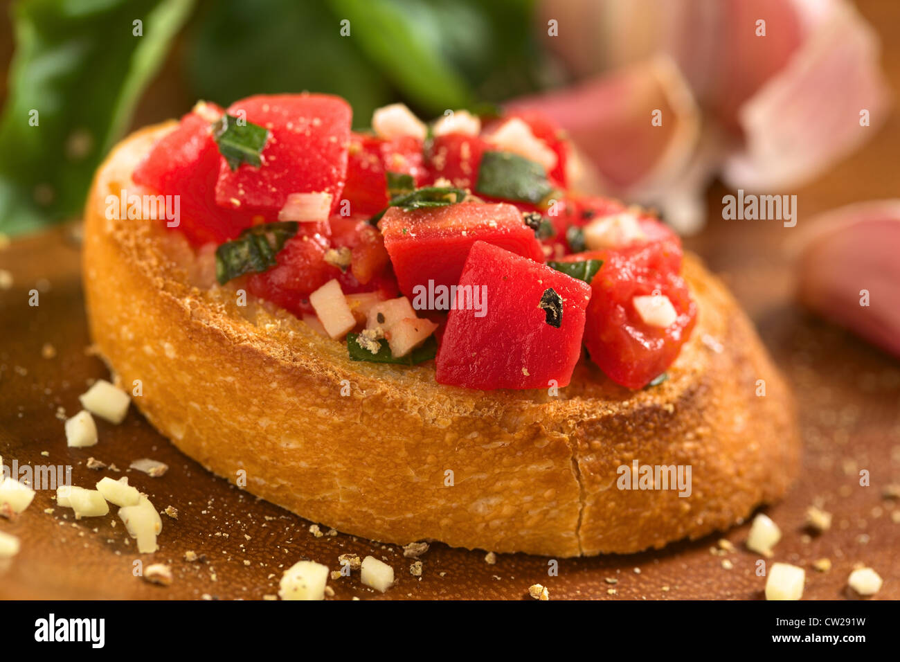 Fresh homemade crispy Italian antipasto called Bruschetta topped with tomato, garlic and basil on wooden board Stock Photo
