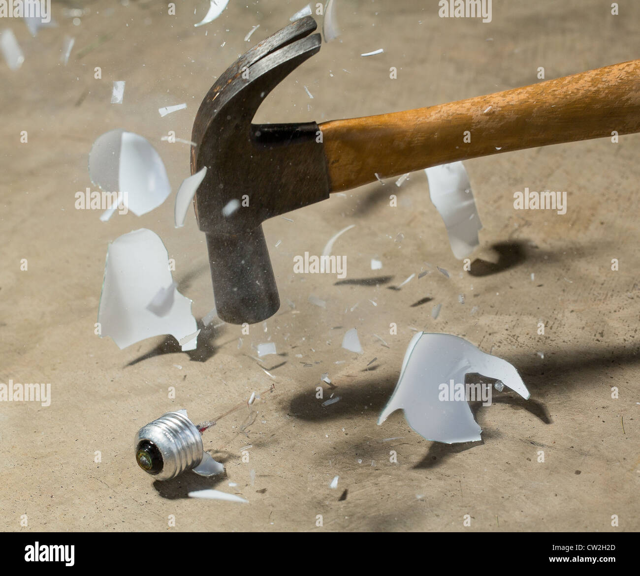 Steel hammer striking glass of incandescent light bulb and smashing it