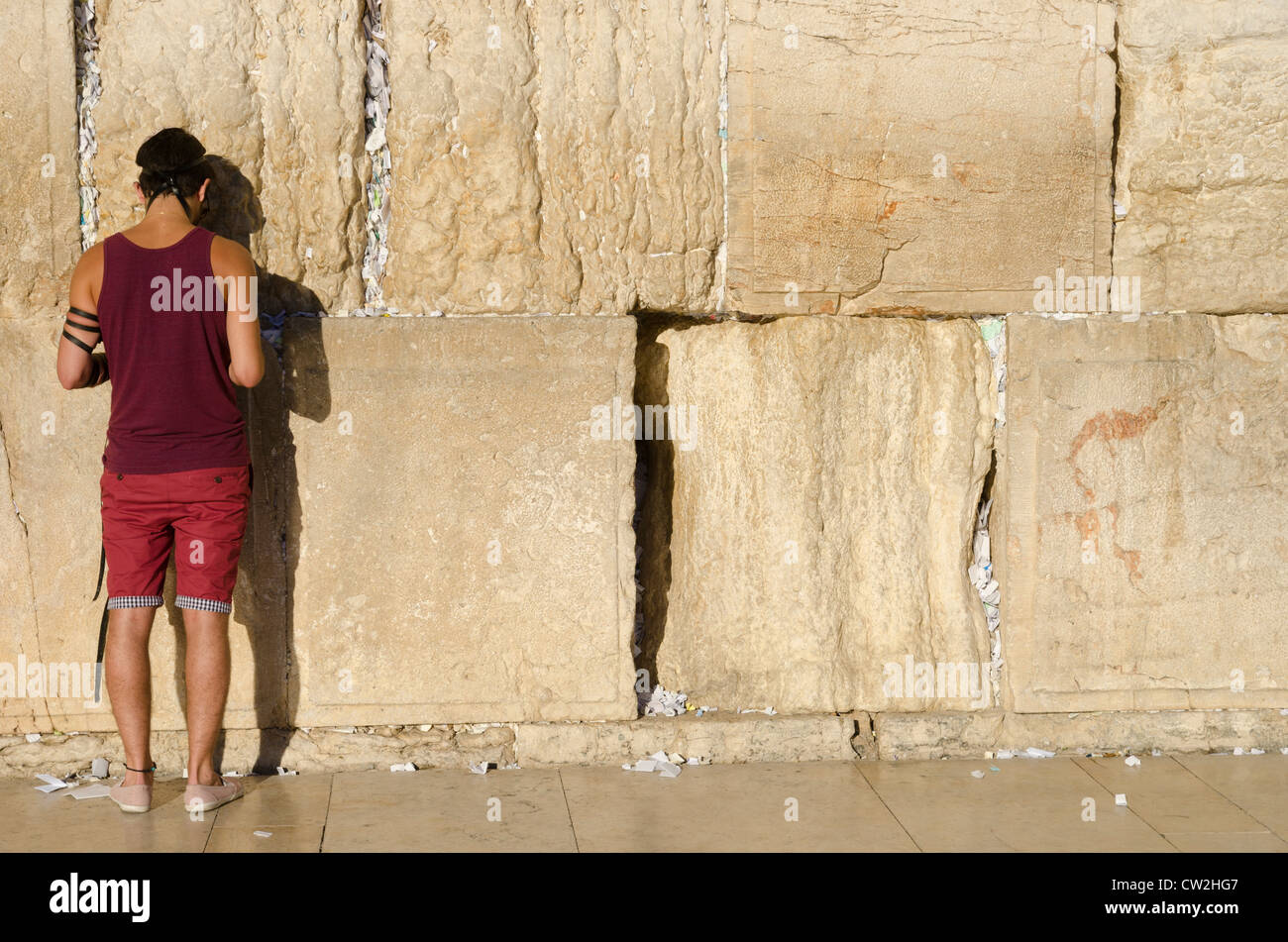 Young jewish man in shorts praying with philacteries at the Western Wall. Jerusalem Old City. Israel. Stock Photo