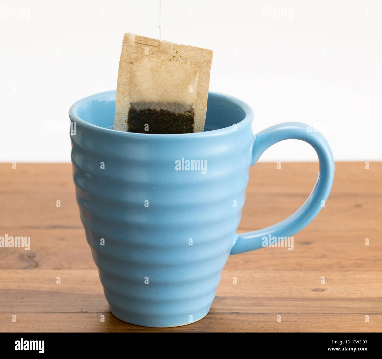 Organic green tea or herbal tea being lowered into a blue mug on wooden table Stock Photo