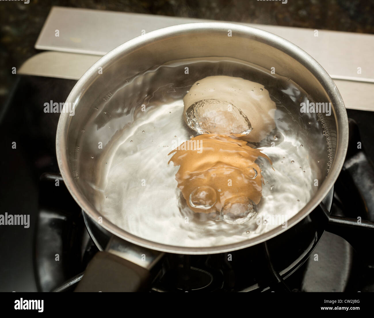 Two eggs in boiling water in stainless steel pan on gas hob Stock Photo