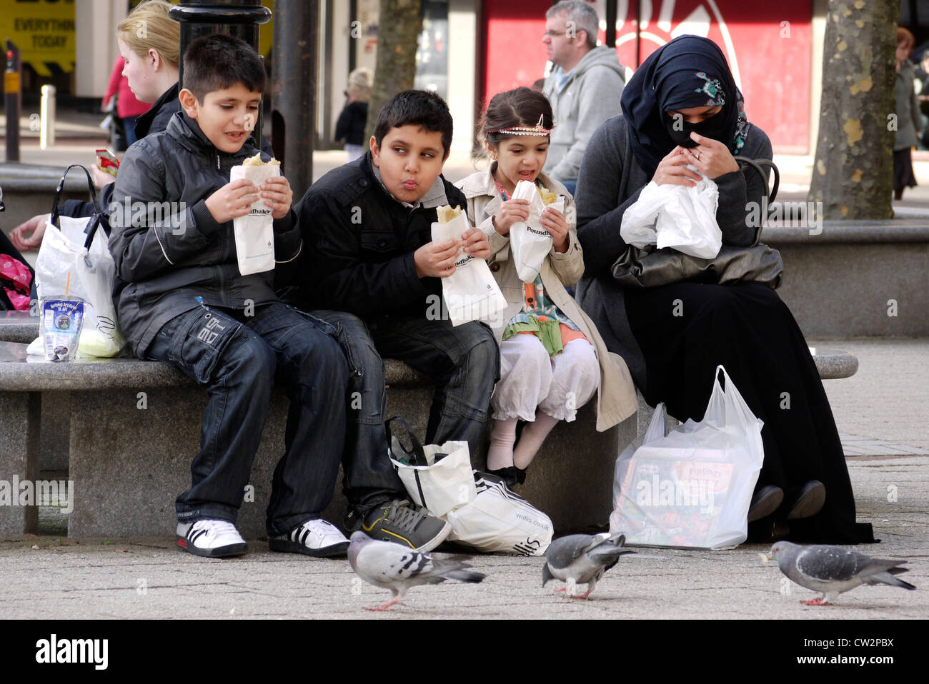 Asian family eating  pasties on Victoria Square precinct in Bolton Lancashire / Greater Manchester UK Stock Photo