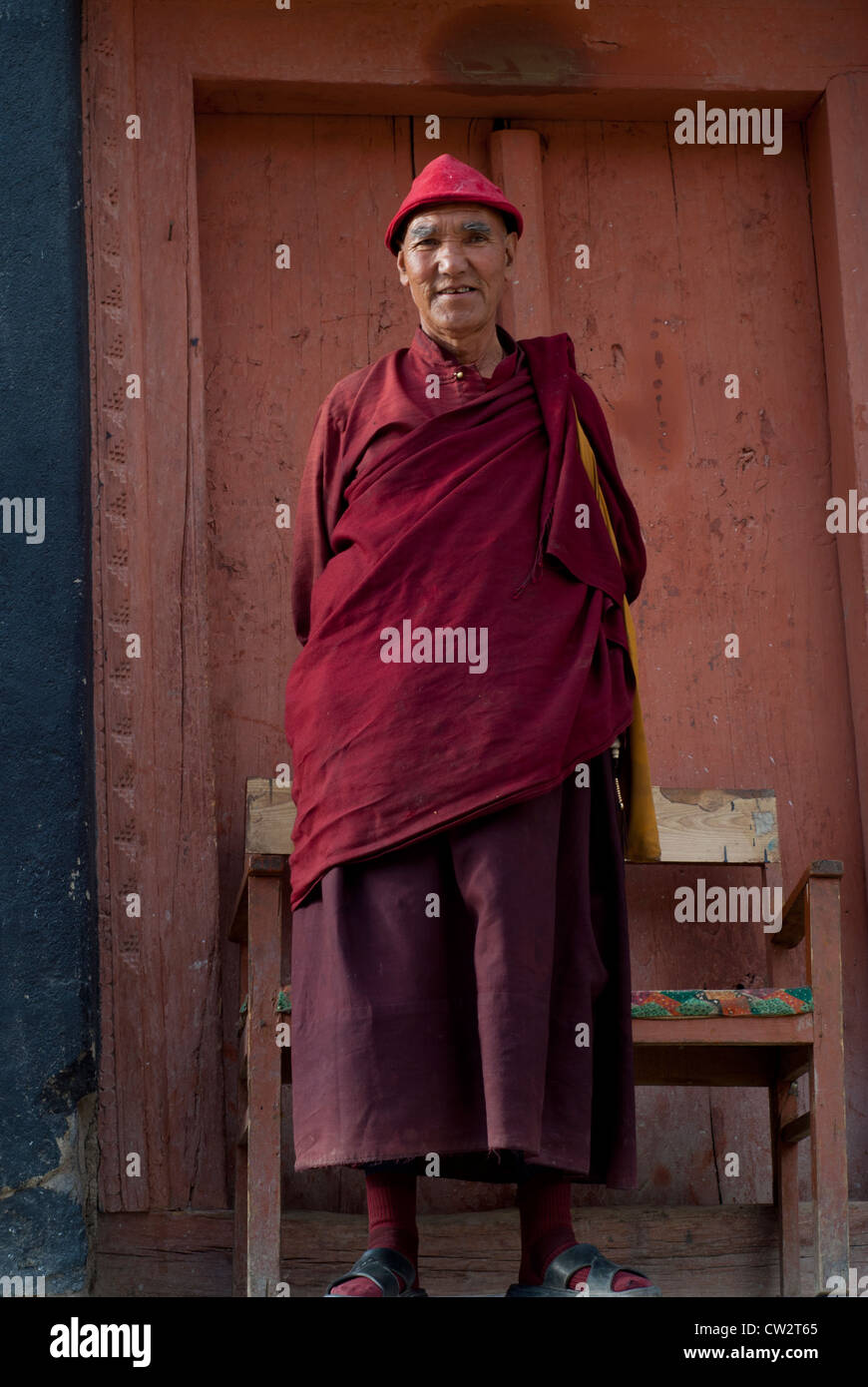 A Tibetan Buddhist monk dressed in traditional red robe with a red hat ...