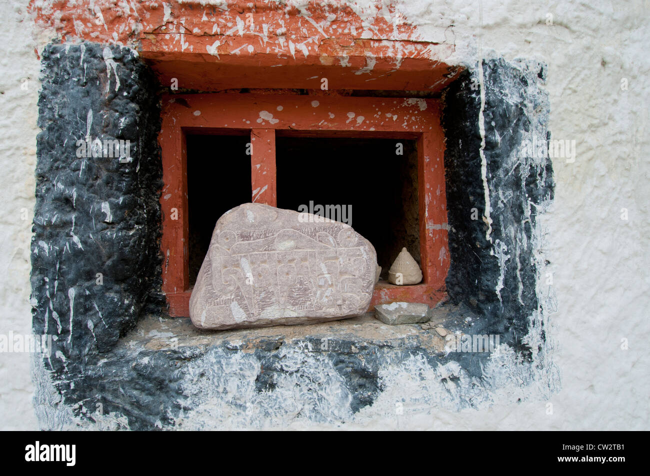 Large and small carved prayer stones on the ledge of a red wooden framed window at Lamayuru Monastery in Ladakh, India Stock Photo