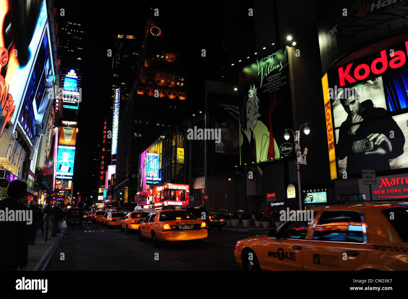 Night neon billboards view, towards 1 Times Square from Disney Store, 6 yellow taxis traffic queue 7th Avenue, New York Stock Photo