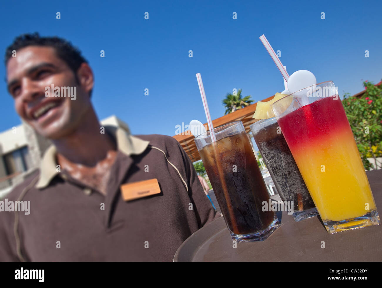 smiling waiter holding a tray of ice cold drinks against a clear blue sky Stock Photo