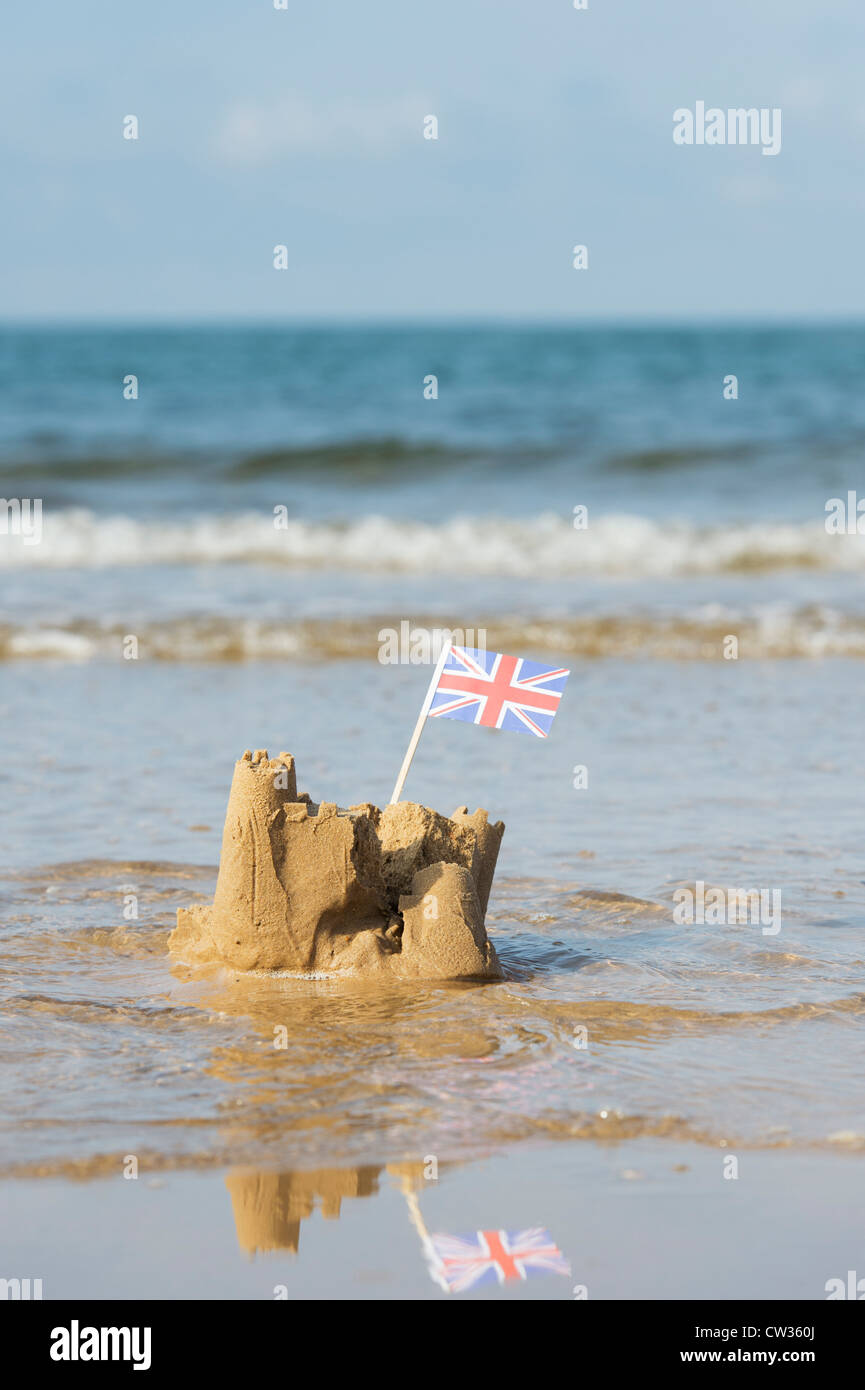 Union Jack flag in a sandcastle being washed away by the sea. Wells next the sea. Norfolk, England Stock Photo