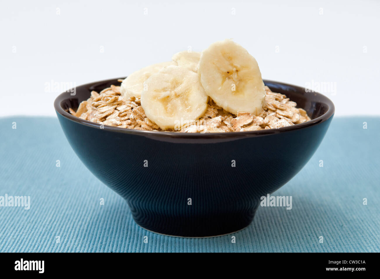 Rolled oats, or porridge oats with sliced banana on top in black bowl Stock Photo