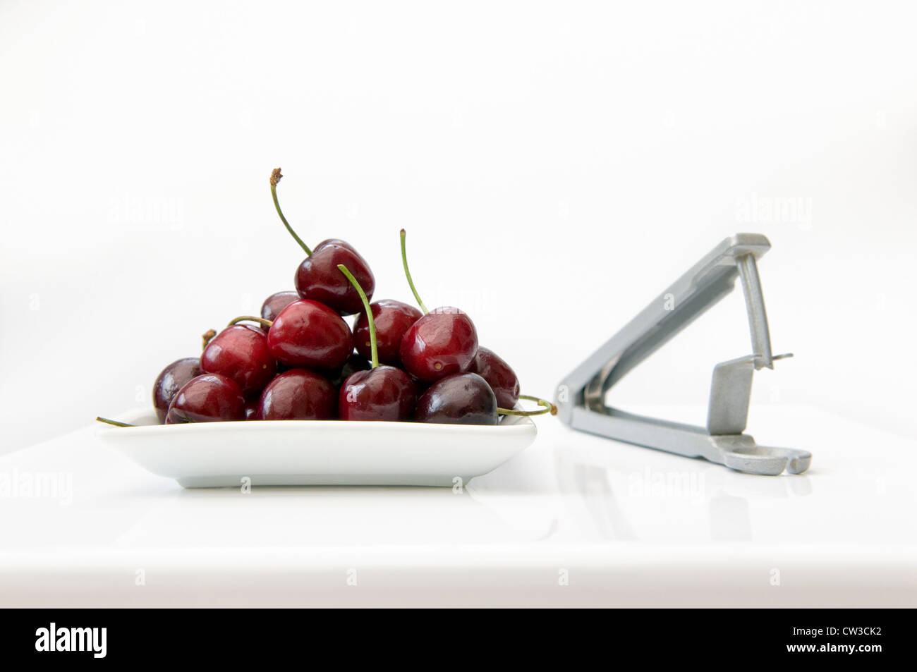 Ripe cherries in white bowl on white table with cherry stoner Stock Photo
