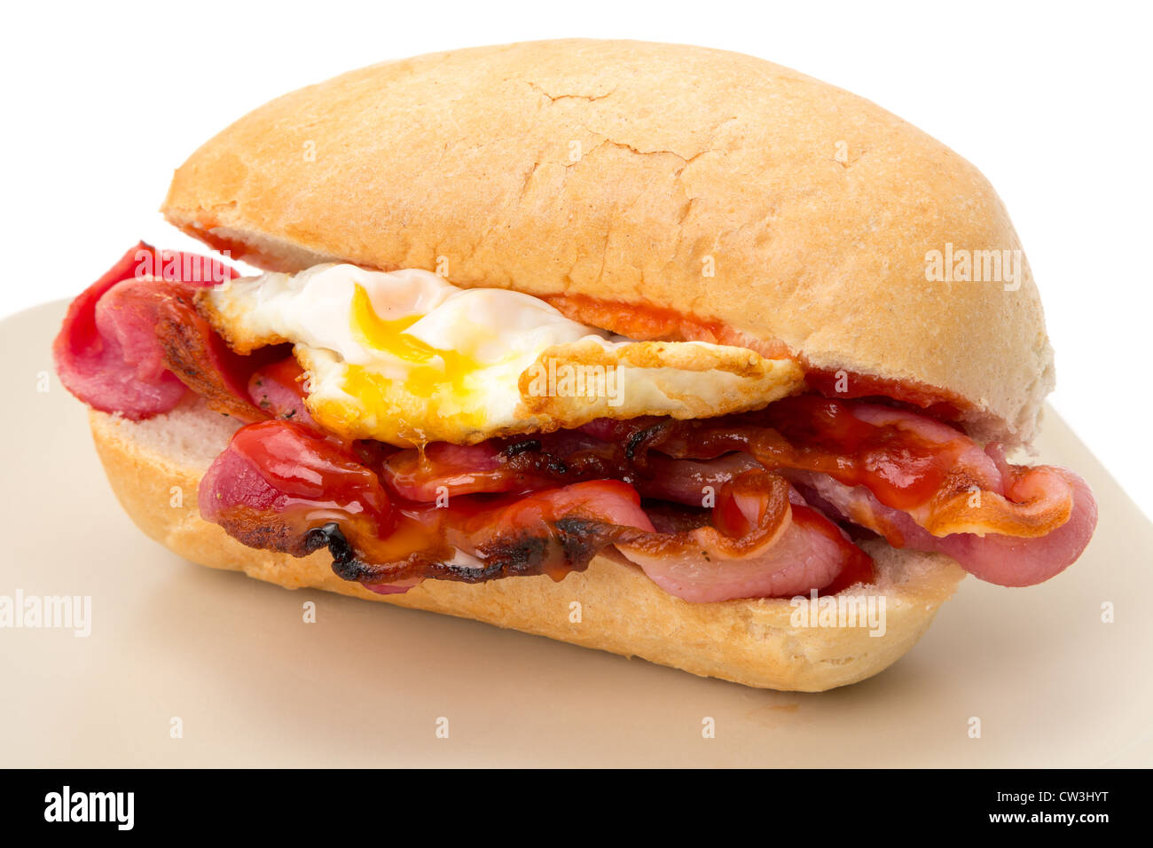 Crispy bacon and a fried egg with tomato ketchup in a bread roll - shallow depth of field - studio shot with a white background Stock Photo