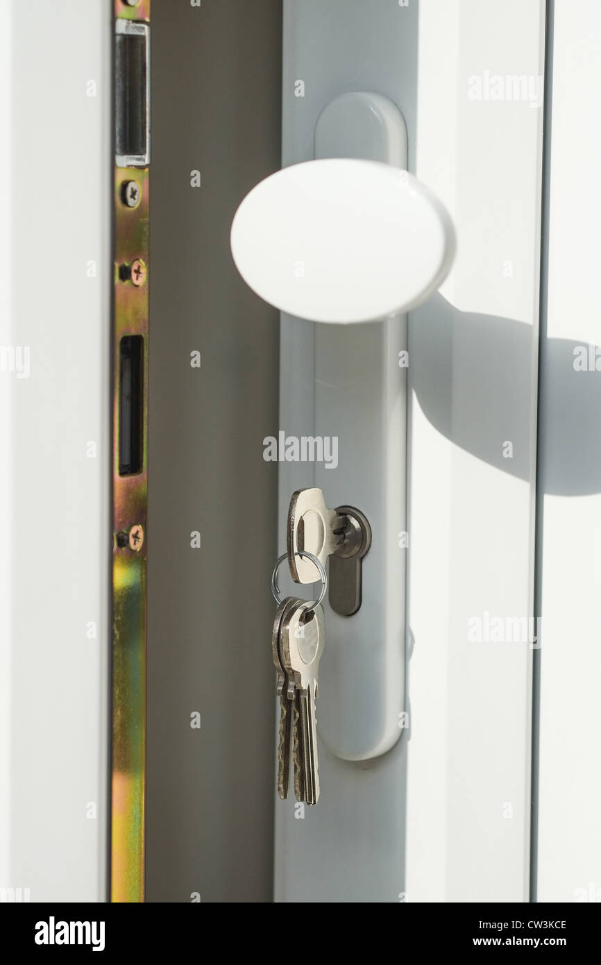 Close-up shot of an open white upvc double glazed door with keys in the lock - brightly lit with a shadow. Stock Photo