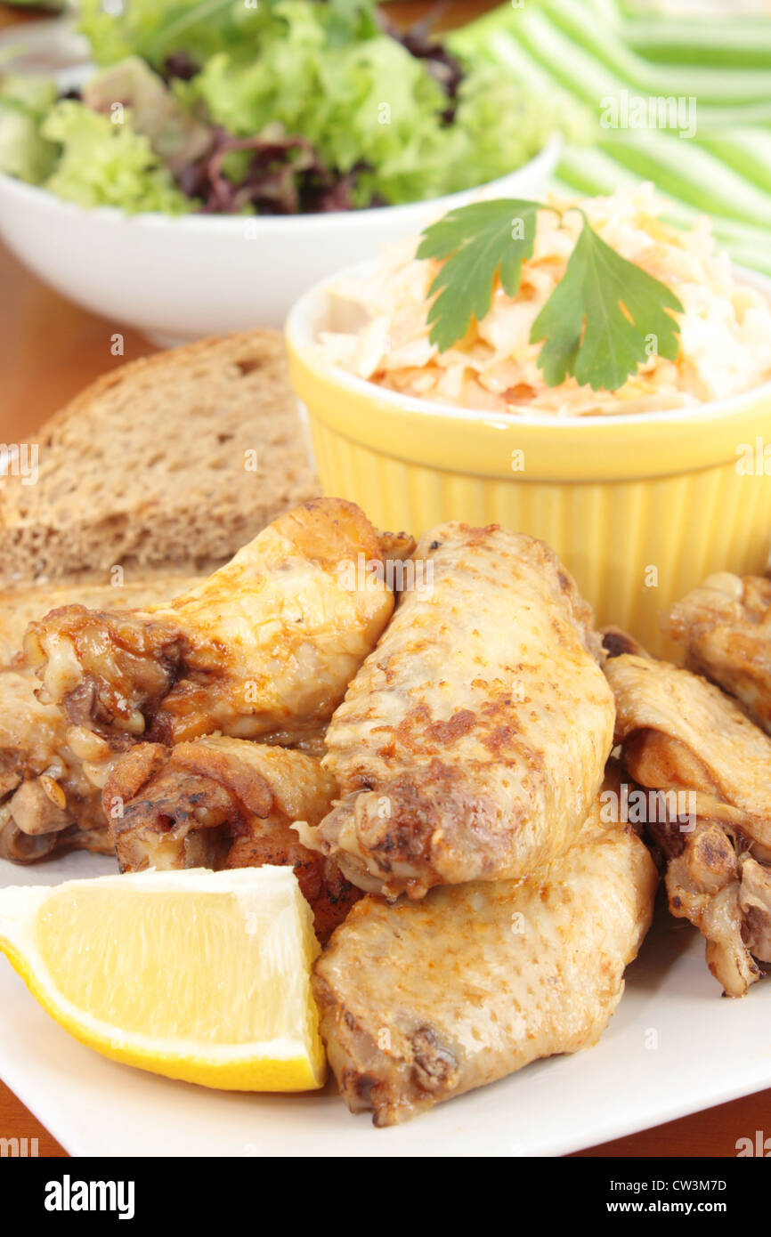 Chicken wings with a dish of coleslaw, brown bread and salad. Stock Photo