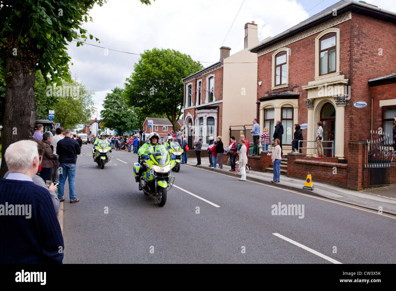 Crowds line New Road, Willenhall, West Midlands to await the passing of the Olympic Torch and its bearer lead by the police Stock Photo