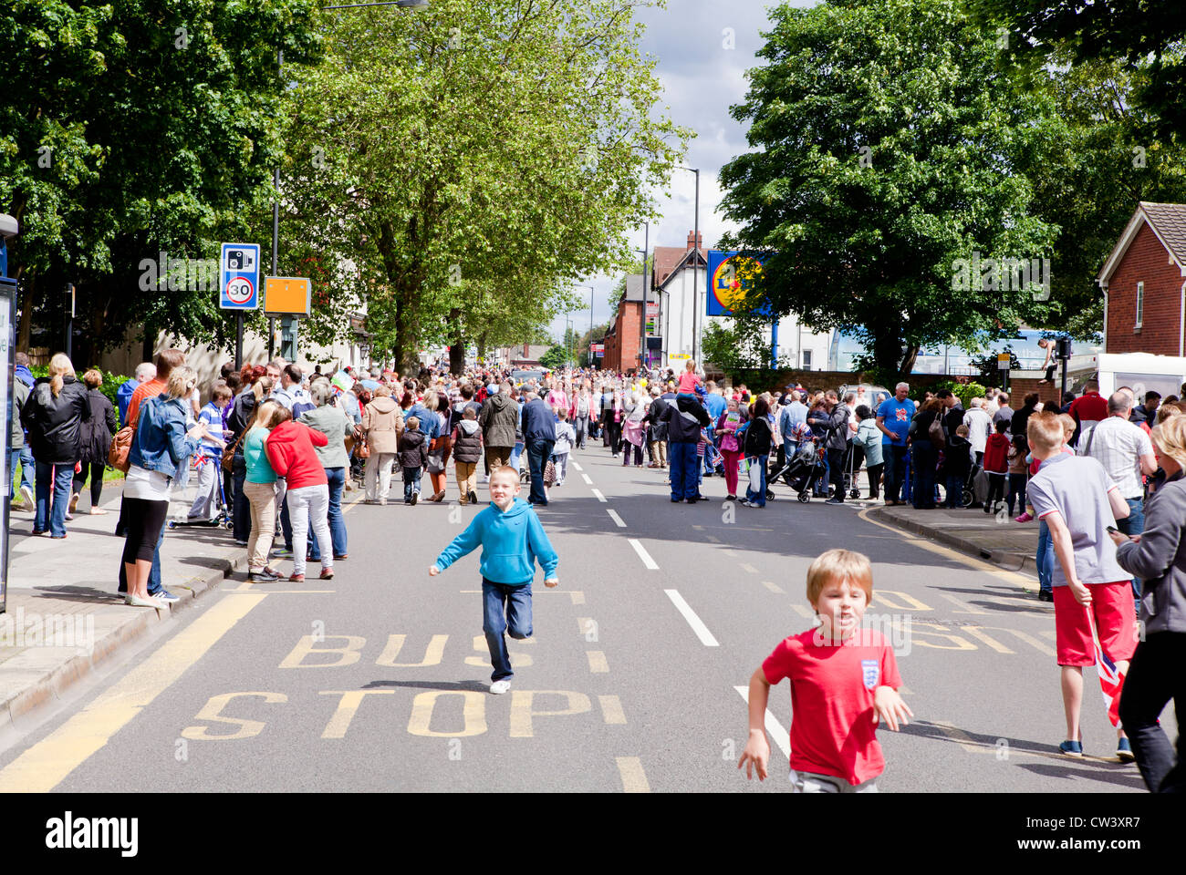 Crowds disperse and young children run towards the passing torch bearer of the Olympic Torch on New Road, Willenhall Stock Photo