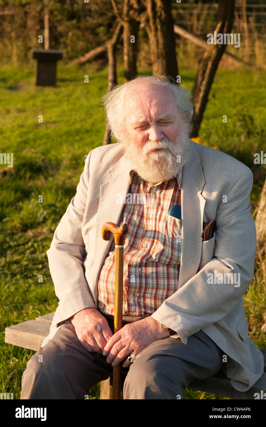 Elderly gentleman sat on bench in country park enjoying evening sunshine looking at camera Stock Photo