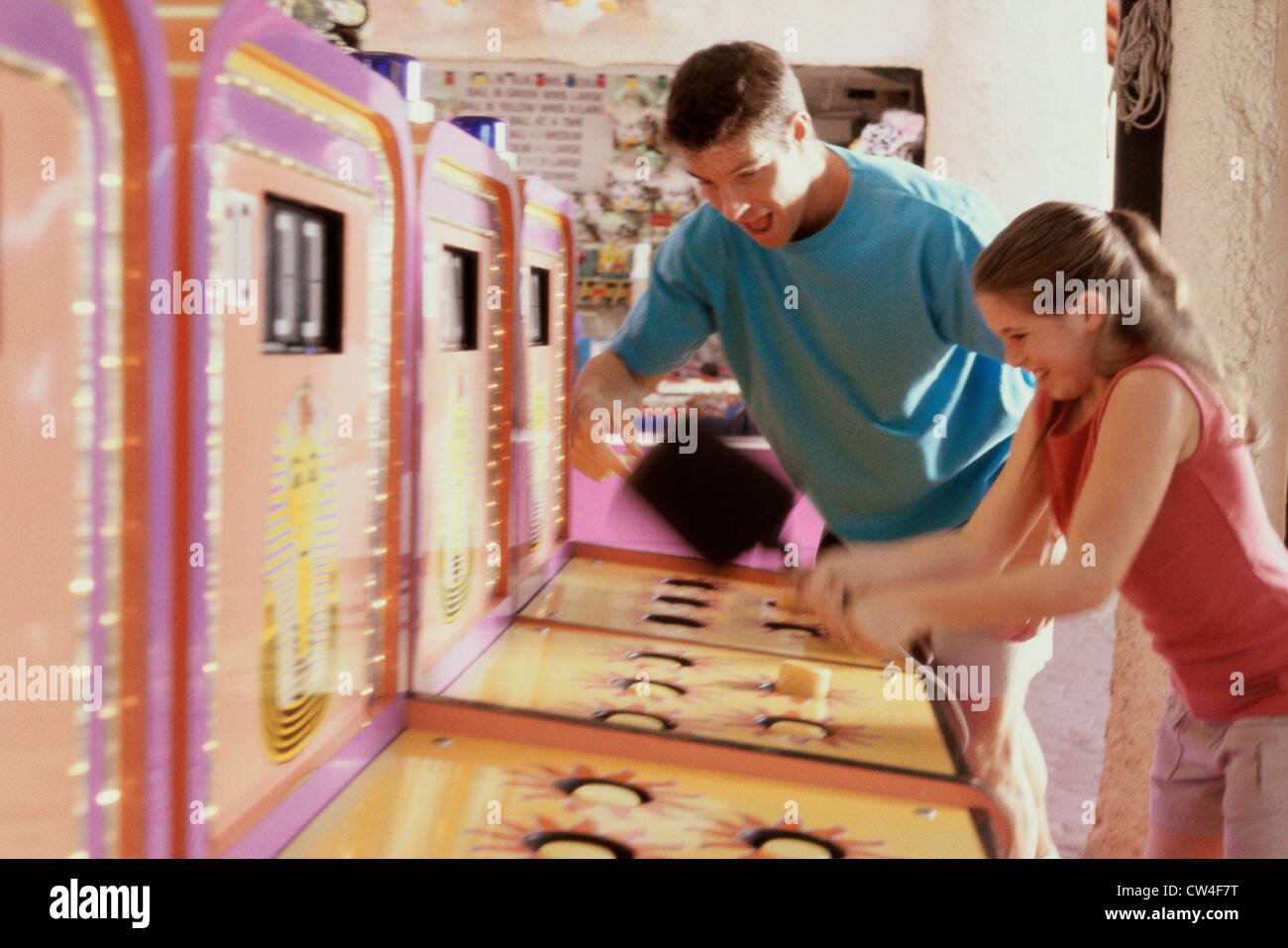 Daughter playing games with her father standing beside her in an amusement park Stock Photo