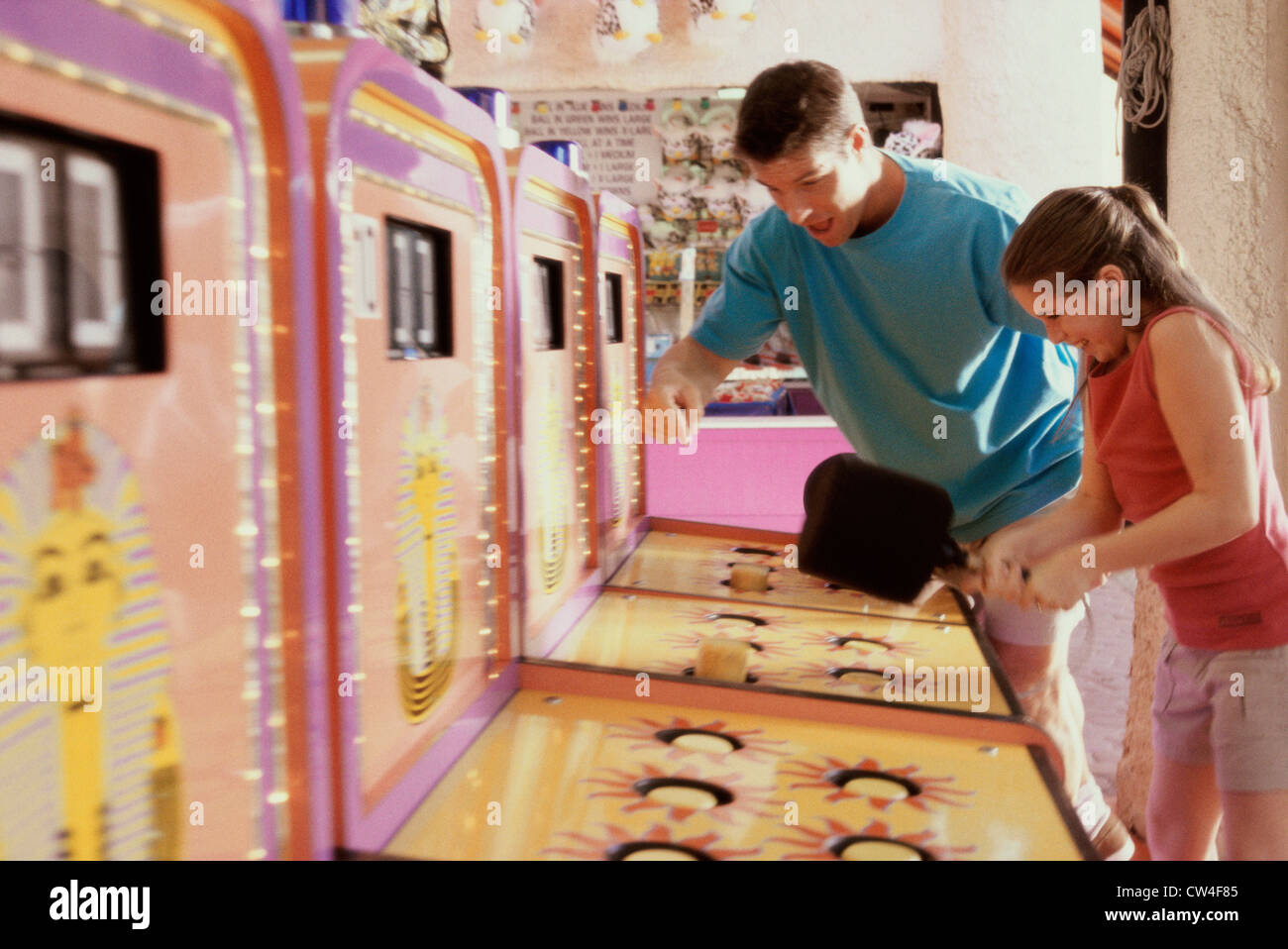 Daughter playing games with her father standing beside her in an amusement park Stock Photo