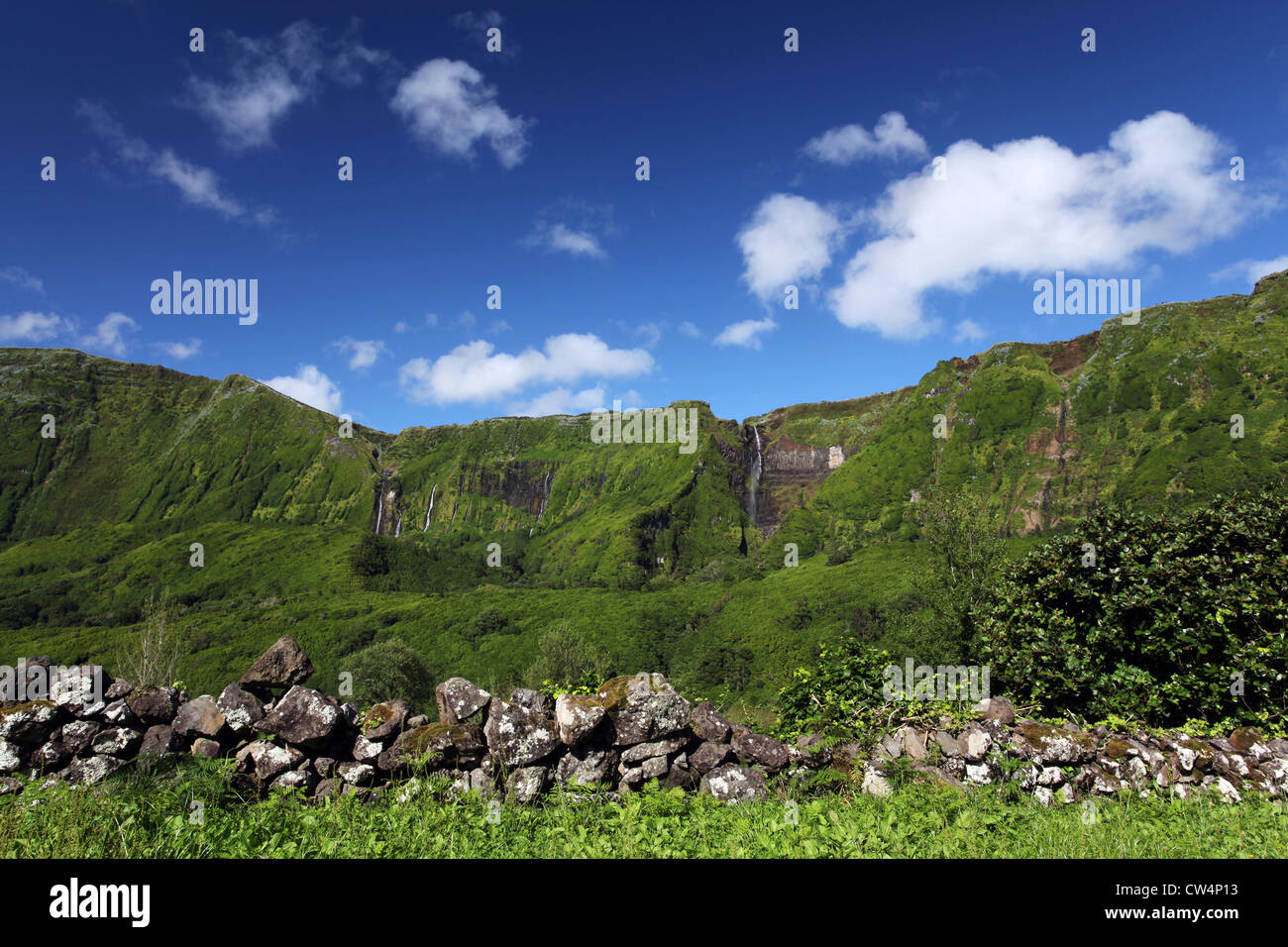 A wall made of basalt rock near Fajazinha surrounded by lush dense vegetation with several waterfalls in the background. Stock Photo