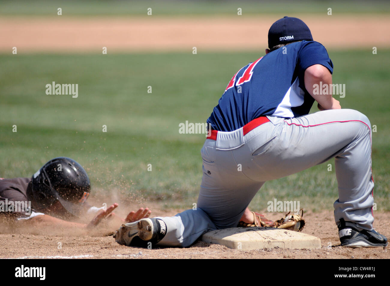 Third baseman receives a throw blocking the runner that is sliding head first into third base. USA. Stock Photo