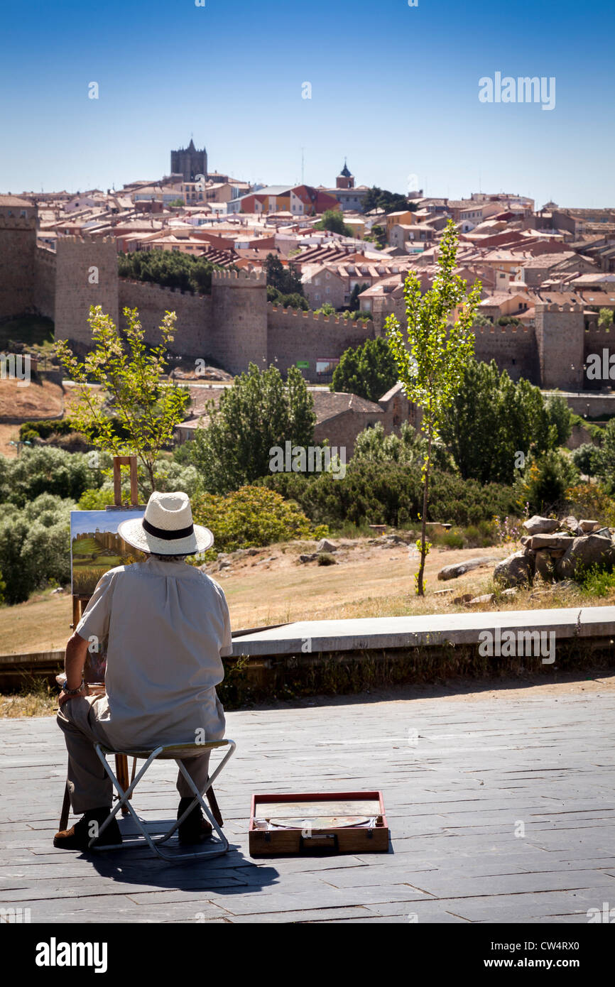 Artist sat painting a scene of the fortification to the medieval city walls of Avila under a clear blue sky, Spain. Stock Photo