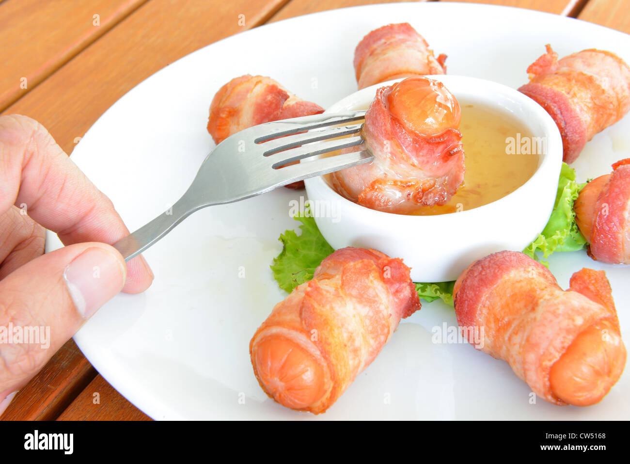 The male hand use fork pick Deep fired sausage wrapped with bacon into sauce. Stock Photo