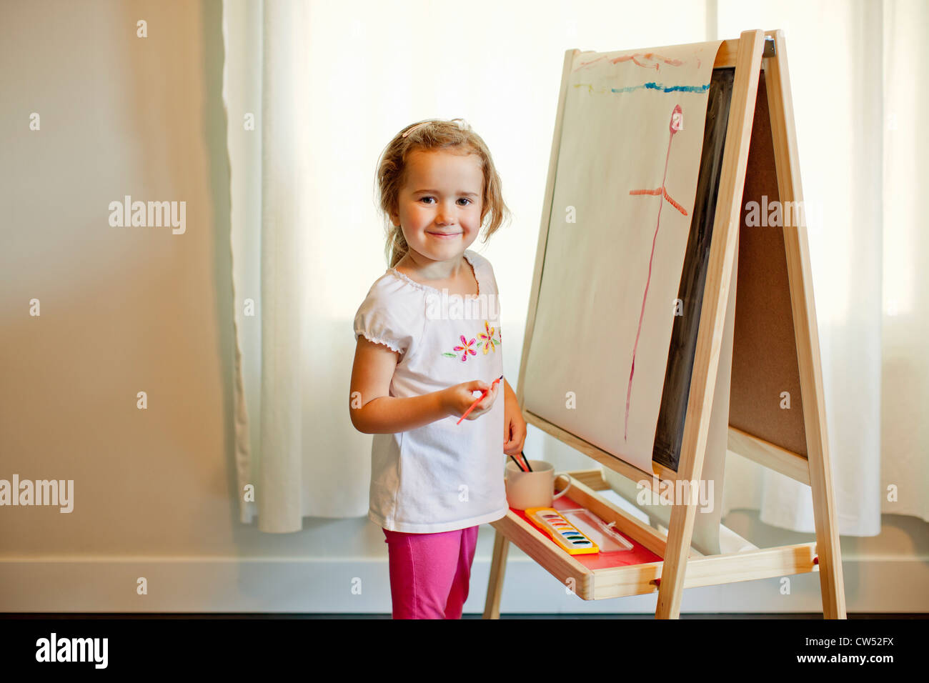 Girl with paint brush standing in front of art on easel Stock Photo - Alamy