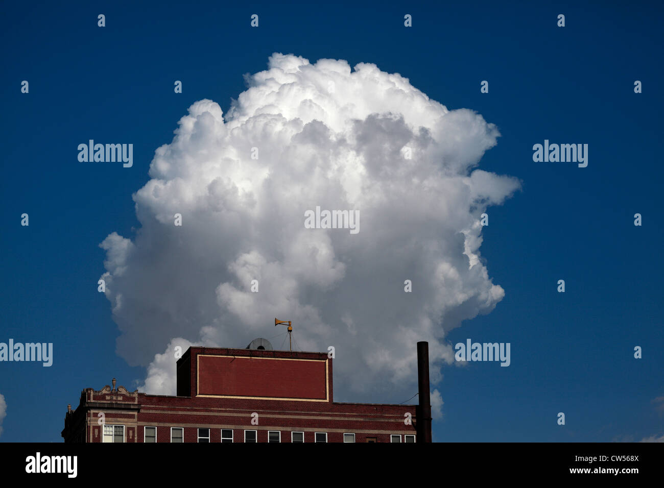 A cumulus cloud rising into the air above & behind a building with an alert siren. Stock Photo