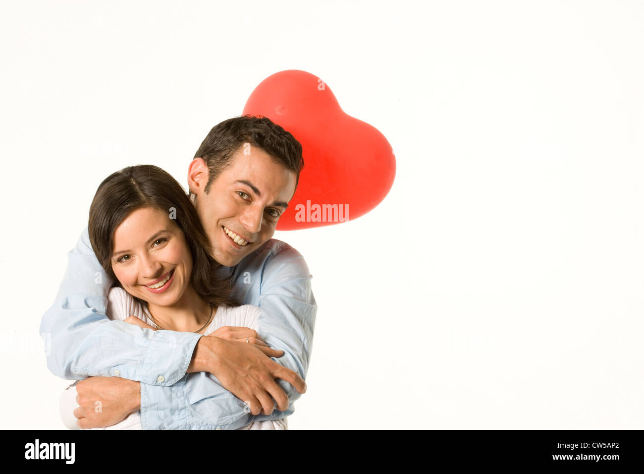 Portrait of a young couple smiling with a heart shape balloon behind ...