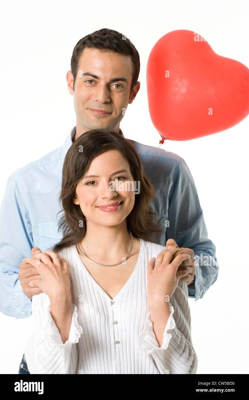 Portrait of a young couple smiling with a heart shape balloon behind ...