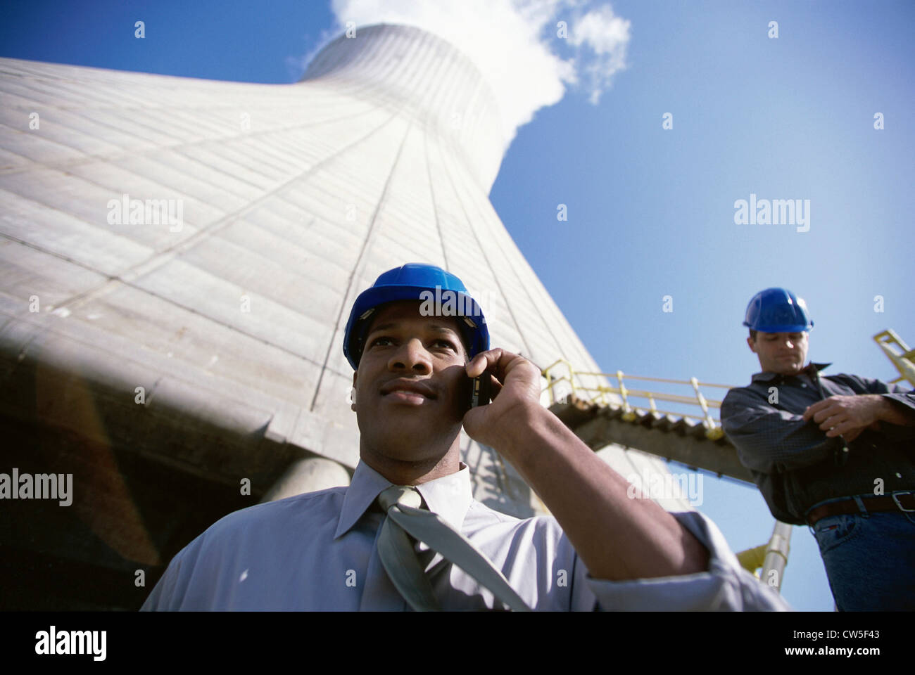 Low angle view of workers standing beside a smoke stack at a power plant Stock Photo