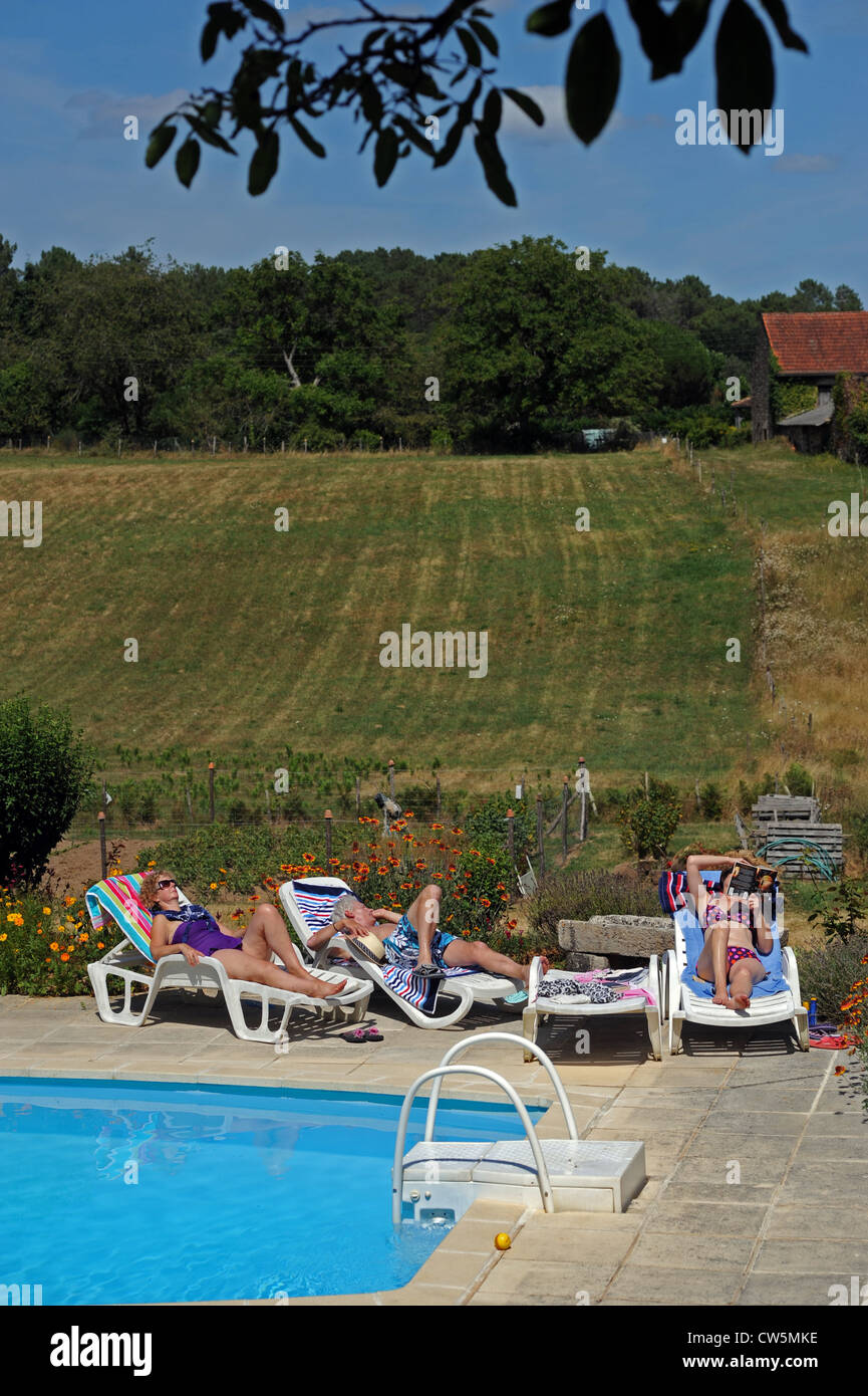 Group of middle aged adults male and female sunbathing by swimming pool at a holiday gite in the Lot Region of South West France Stock Photo