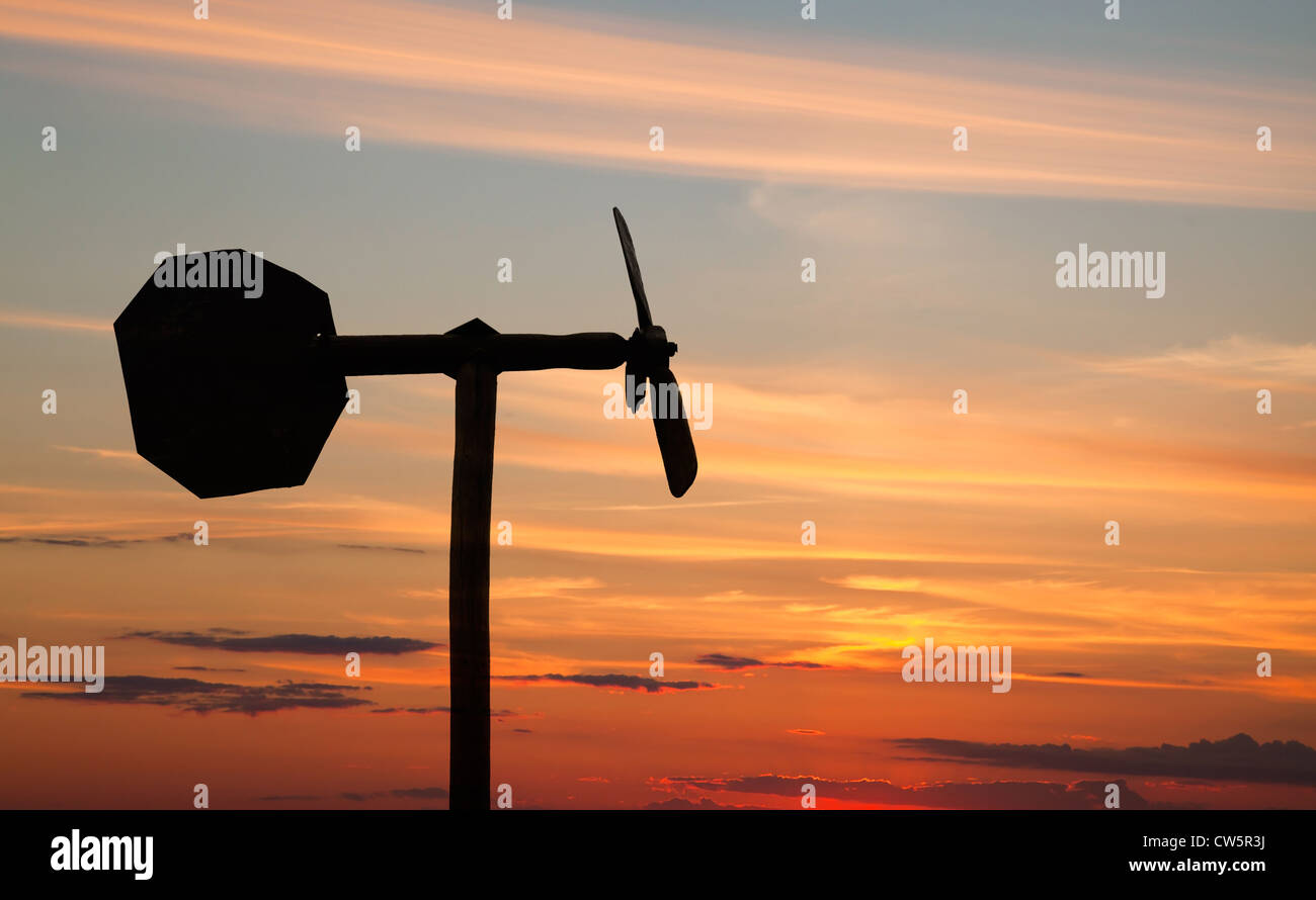 Small windmill style weather vane silhouette above orange sunset sky Stock Photo