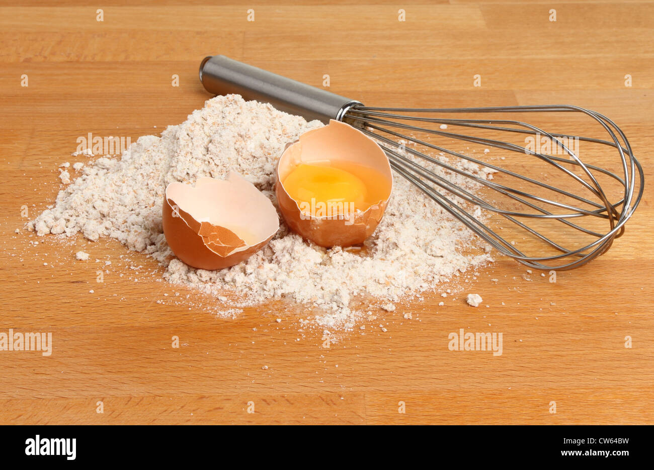 Wholegrain flour with a cracked egg and whisk on a wooden worktop Stock Photo